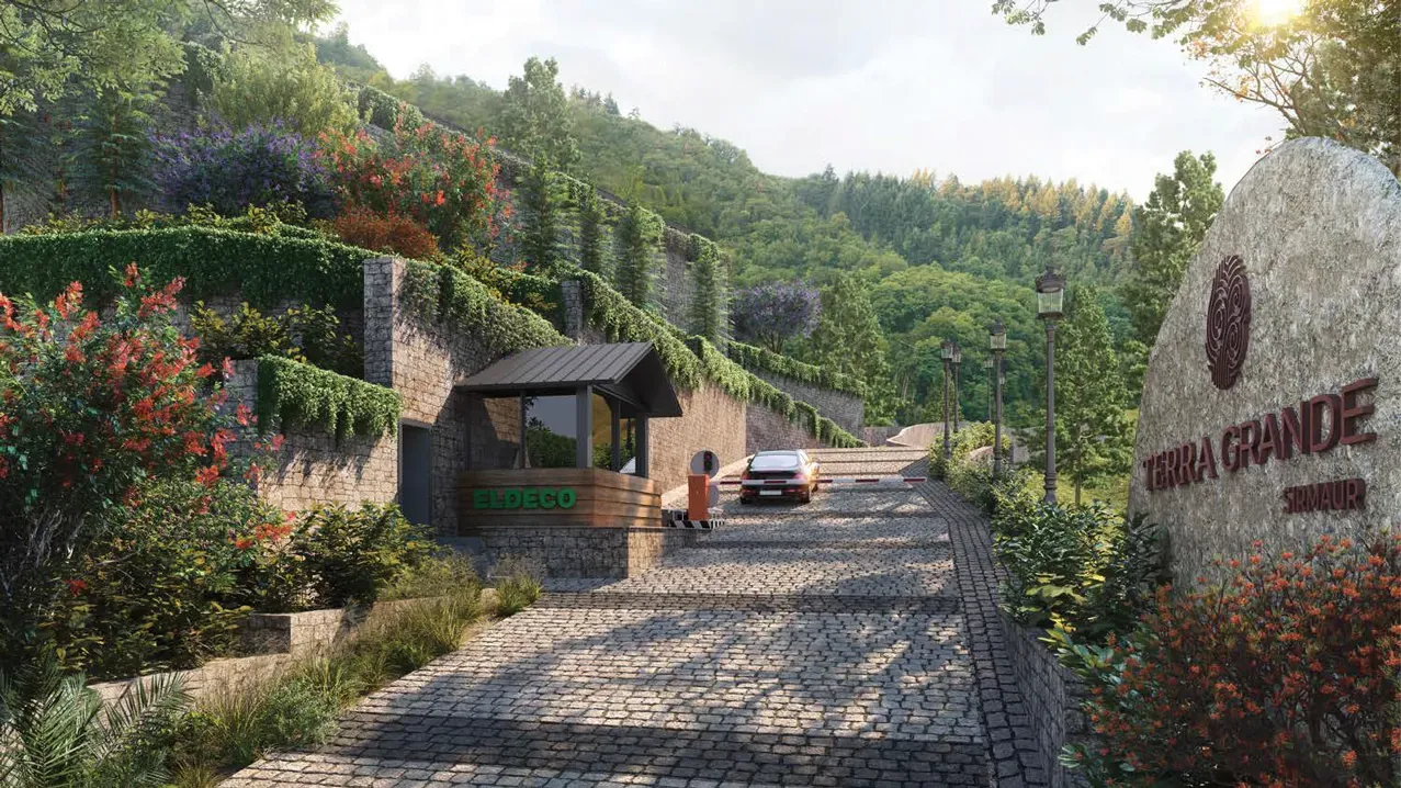 The arrival at Eldeco Terra Grande: a stone-paved driveway climbing past the carved Terra Grande marker stone, flowering hedges and the gatehouse